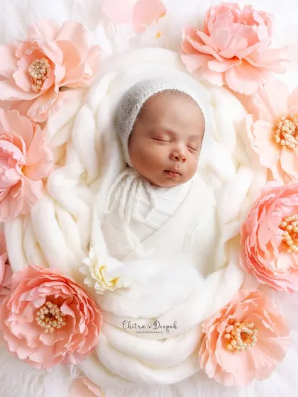 A delicate newborn portrait showing a baby nestled in soft white wraps, encircled by beautiful pink peonies. We focus on creating serene and timeless images, paying close attention to every soft detail.