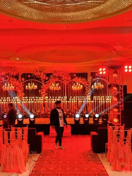 We use professional lighting to completely change the mood of a space. Here, a sangeet stage is bathed in dramatic red light, with intricate candle walls and spotlights creating a high-energy, club-like atmosphere perfect for a night of dancing.