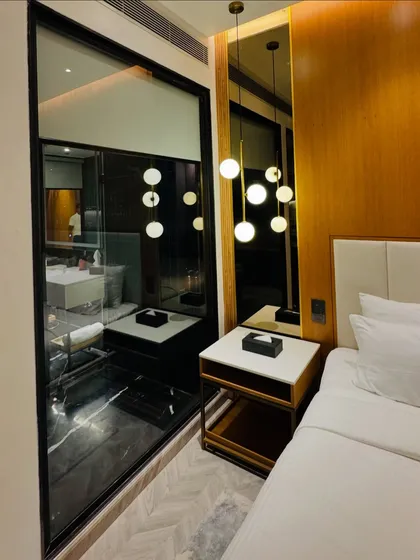 We inspect guest accommodations to ensure quality. This image shows a modern hotel room with stylish lighting, a comfortable bed, and a clear view into the well-appointed bathroom.