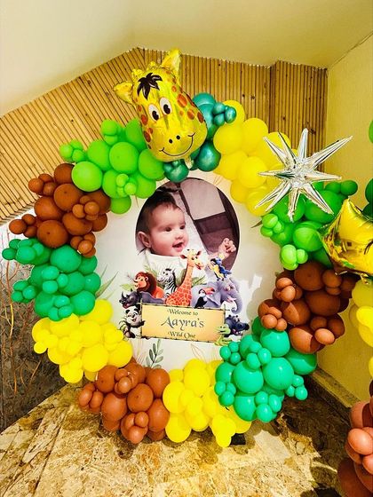 A custom welcome sign for 'Aayra's Wild One' party, framed by a circular balloon arrangement and a giraffe foil balloon.