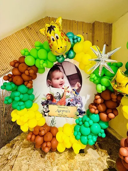 A custom welcome sign for 'Aayra's Wild One' party, framed by a circular balloon arrangement and a giraffe foil balloon.