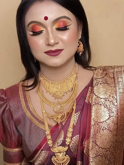 A dramatic and traditional bridal look. The sunset-toned eyeshadow with orange and red hues creates a fiery effect, perfectly matched with a deep maroon lipstick and heavy gold jewelry.