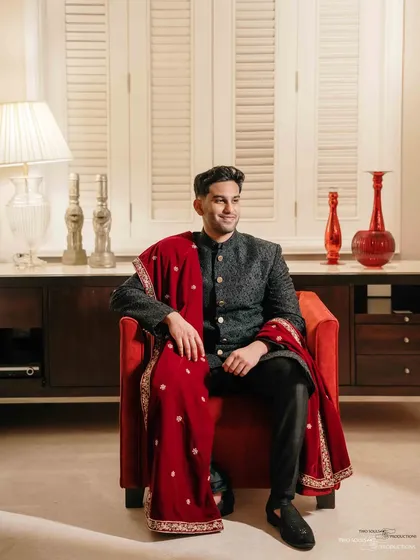 A confident and smiling portrait of the groom. Seated in a bold red chair, his personality shines through in this stylish and well-lit shot.