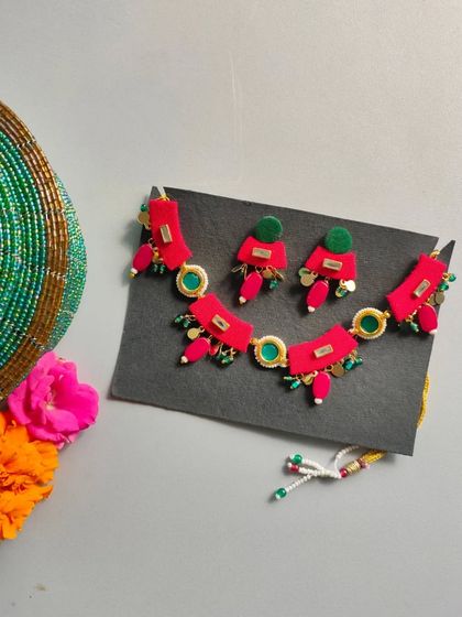 A vibrant red and green necklace set perfect for a Mehendi or Haldi ceremony. The design uses fabric pieces and beads to create a colorful, floral-inspired look.