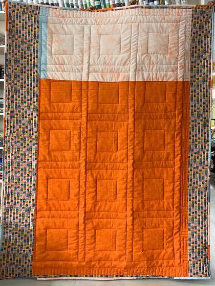 The back of the quilt, pieced with bright orange and patterned fabric.