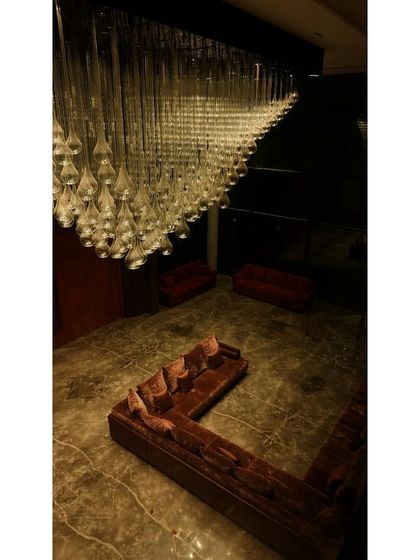 A dramatic, top-down view of a custom chandelier in a formal living area. The lighting is designed to be the main feature in the dark, moody space, casting a beautiful, warm glow over the seating area below.