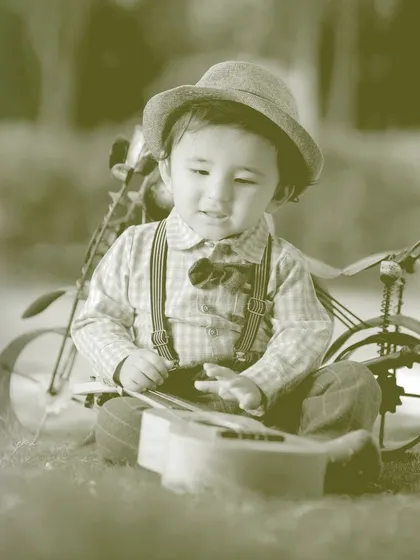 A creative, sepia-toned photo of a boy playing with a toy guitar, showing our ability to apply different artistic styles to your photos.