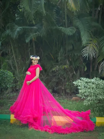 A stunning solo shot showcasing the long, dramatic train of the fuchsia gown against a lush green backdrop.