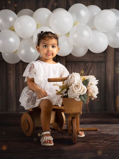 A beautiful portrait of a little girl on a wooden tricycle, taken during a celebrity family shoot. The rustic props and simple white dress create a timeless look.