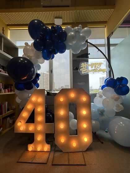 A 40th birthday party setup in an office, showing the large marquee numbers and balloon arch against a window with a city view.
