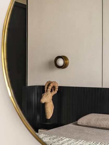 A detail shot from Apartment 3201, where a carved wooden artifact is reflected in a brass-framed mirror. This composition of textures, from the fluted black headboard to the smooth metal, exemplifies our focus on creating curated, artful moments.