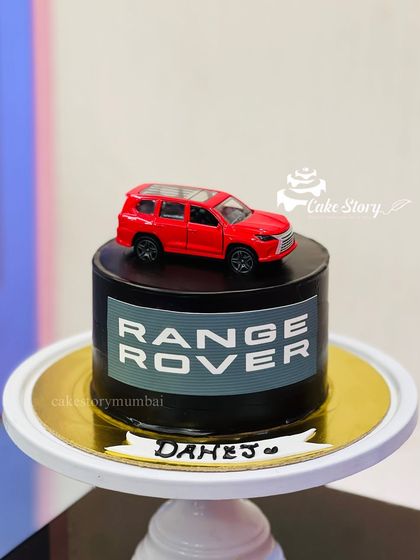 A sleek and simple Range Rover cake. The black cake features the brand's logo and is topped with a miniature red Range Rover model.