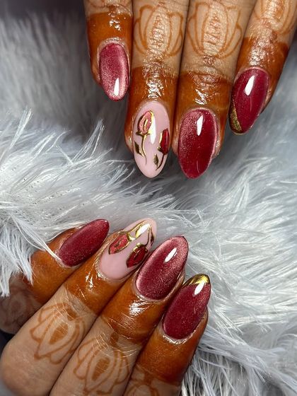 A romantic bridal look with shimmering burgundy cat eye nails and accent nails featuring soft pink with gold-detailed roses.