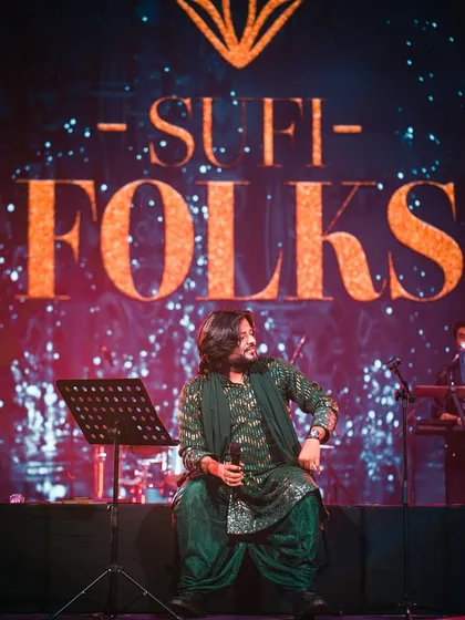 Seated on stage against our signature backdrop, this image captures a moment of reflection between songs. It shows the calm and composed nature of our mehfil setup.