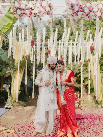 A beautiful portrait of a Marathi couple standing under a mandap decorated with fragrant tuberose garlands.