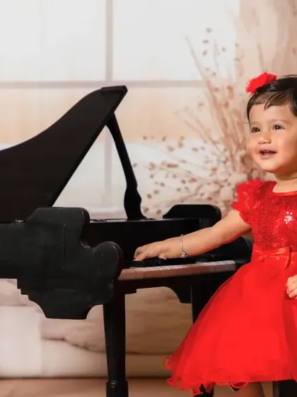 A happy girl in a red dress, playing a tune on the black piano.