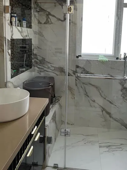 This angle shows the layout of the marble bathroom, including the glass shower partition and the niche for toiletries, all designed for a clean and uncluttered look.