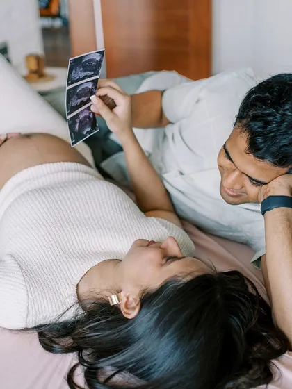 A different angle of the couple looking at their ultrasound scan. This shot shows his perspective as he looks down at the image with her, sharing the moment of discovery.
