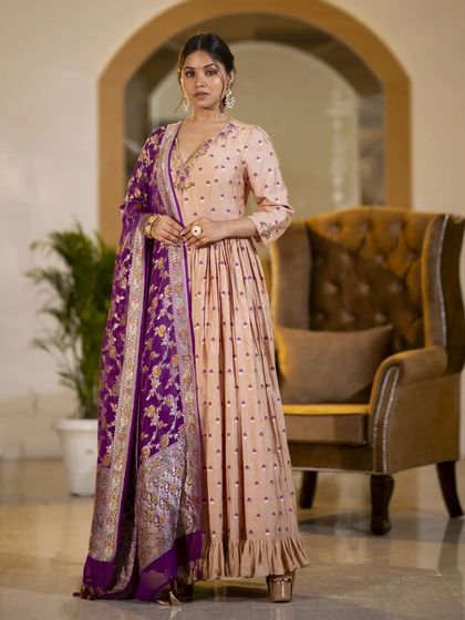 A model wearing a beautiful beige Anarkali gown with a contrasting purple Banarasi dupatta. This image showcases a complete ethnic ensemble, emphasizing the rich color combination and traditional weave.