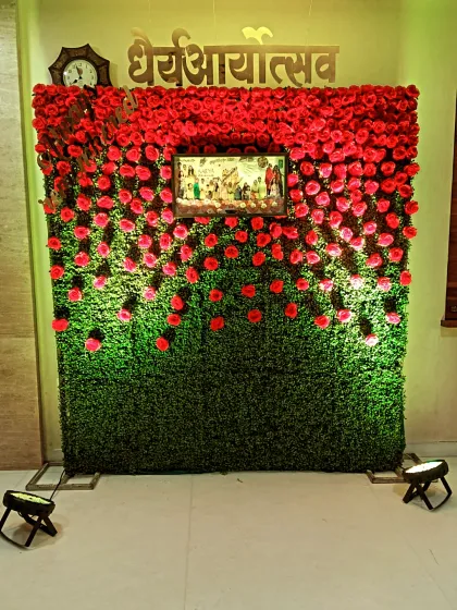 A unique wall decoration featuring a green grass backdrop covered in red roses. A framed picture is placed in the center, making it a personalized tribute for a cultural event.