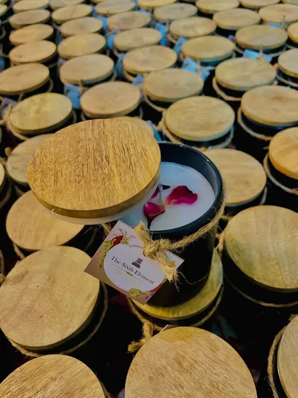 This black jar candle, featuring a wooden lid and a custom tag for "The Sixth Element," is part of a large corporate order. We use high-quality soy wax and top it with real rose petals for a touch of elegance.