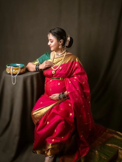 A traditional maternity photoshoot in a pink saree, capturing a moment of quiet contemplation and beauty.