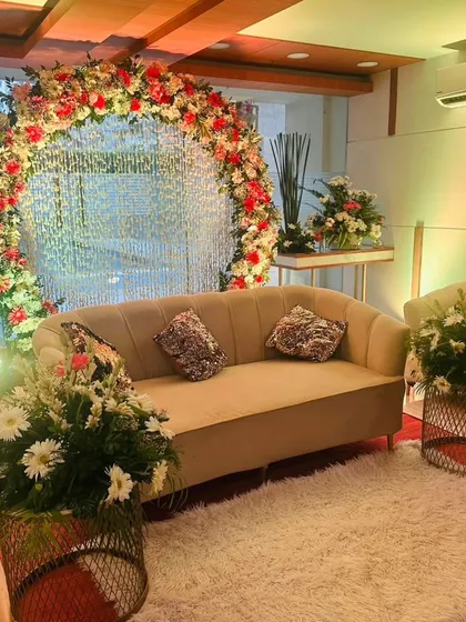 A cozy and elegant seating area for a Roka or engagement ceremony, featuring a circular floral arch with a crystal curtain backdrop, comfortable sofas, and plush carpeting.