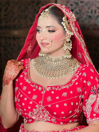 A close-up on the blouse and jewelry of a bride in a red lehenga. Notice the detailed peacock embroidery on the sleeves and the stunning choker necklace.