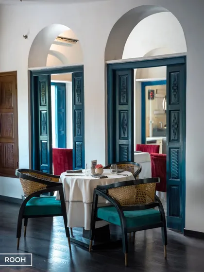 Heritage whispers through our walls. The beautifully carved blue doors and classic cane-backed chairs reflect a blend of traditional craftsmanship and contemporary design.