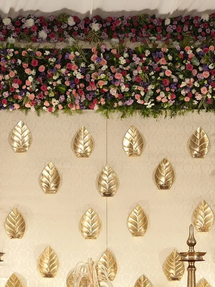 A close-up of the cream and gold backdrop, where golden leaves are mounted on the wall and framed by a dense border of colorful flowers.