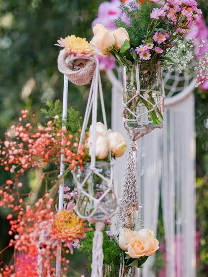 A detail shot of hanging macrame planters holding glass jars filled with peach roses and other delicate blooms.