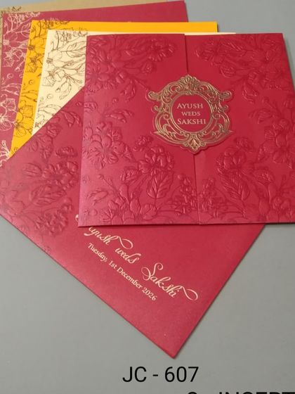 This bright red gate-fold invitation has an embossed texture and an ornate gold emblem. The set includes colorful inserts in yellow and cream for a festive look.