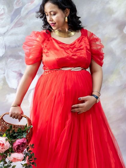 A classic studio portrait of a mom-to-be in a red gown, holding a basket of flowers.