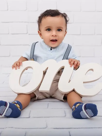 A classic first birthday photo with a simple white brick background and a "one" prop.