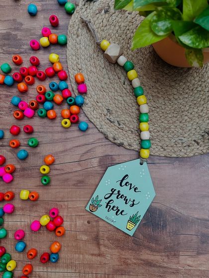 Our 'Love Grows Here' beaded hut is a sweet reminder of the love in your home. This hand-doodled piece with colorful beads is a perfect gift for a loved one or a beautiful addition to your own decor.
