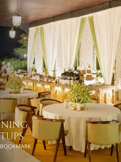 A sophisticated outdoor dining setup for an evening event, with elegant white drapes and a beautifully lit buffet station.