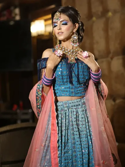 This blue lehenga with a cold-shoulder, fringed blouse is a super trendy option for a sangeet or mehendi. It's paired with beautiful floral jewelry.