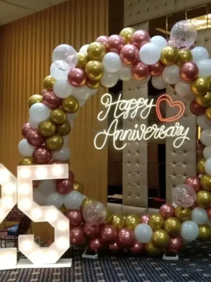 Celebrate a silver jubilee with a stunning photo corner. This 25th anniversary setup combines a circular balloon arch in rose gold, white, and chrome with large, illuminated marquee numbers to highlight your special milestone.
