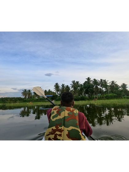 Paddling through the calm waters, with the reflection of the palm trees visible on the surface.