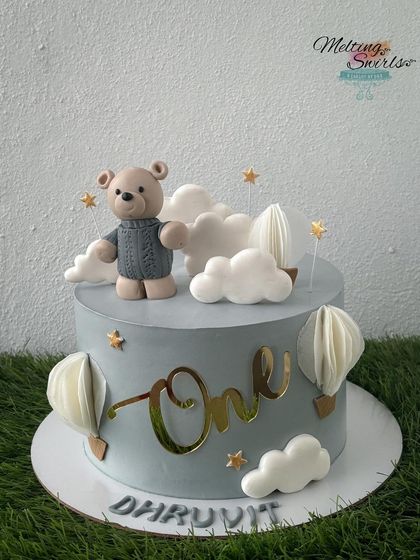 A dreamy cake for a first birthday. This design features a teddy bear, wafer paper hot air balloons, and fondant clouds on a gentle gray whipped cream cake.