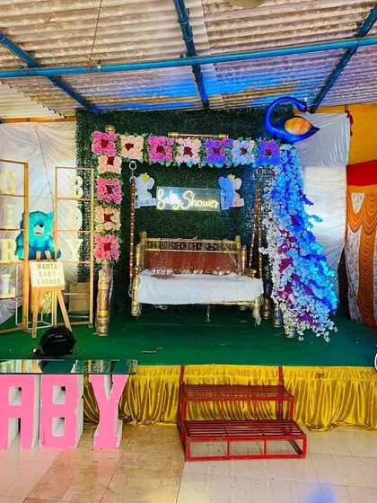 A wide shot of a baby shower stage with Radha and Krishna cutouts, large 'BABY' letters, and a decorated swing.