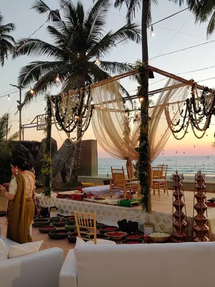 A wider view of the rustic beach wedding, showing the mandap and guest seating. The combination of natural textures, warm lighting, and the sunset creates a truly magical and inviting atmosphere.