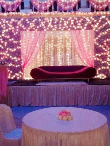 For a dazzling effect, I created this stage backdrop using a full wall of fairy lights behind sheer pink curtains. This setup is perfect for evening events like a sangeet or reception.