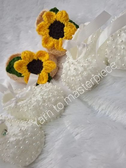 This image shows two beautiful pairs of formal baby shoes: one with a bright sunflower and the other in classic white with pearls.