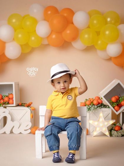 A stylish little boy tips his hat during his cheerful, orange-themed first birthday photoshoot.