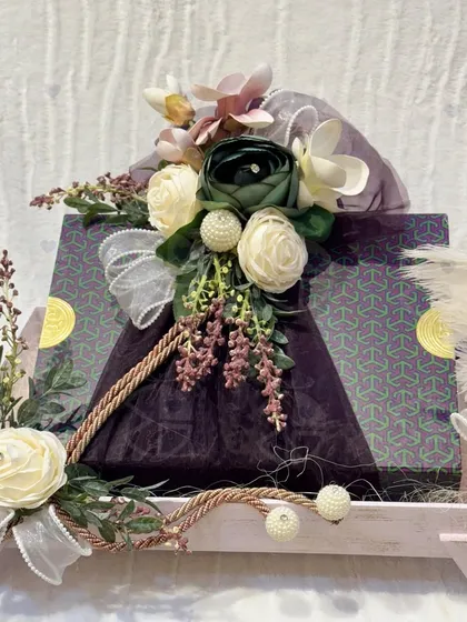A sophisticated wedding gift tray in a soft lavender hue. The gifts are wrapped in a deep purple fabric and adorned with cream-colored sola wood flowers, creating an elegant and unique color combination.