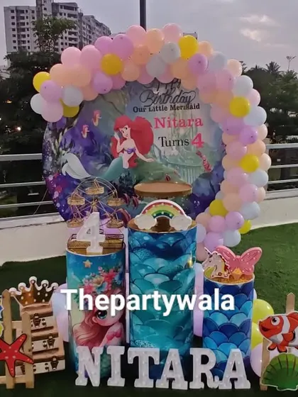A beautiful outdoor Mermaid theme party on a rooftop. The setup includes a full backdrop, character cutouts, and themed props, creating an underwater wonderland with a city view.