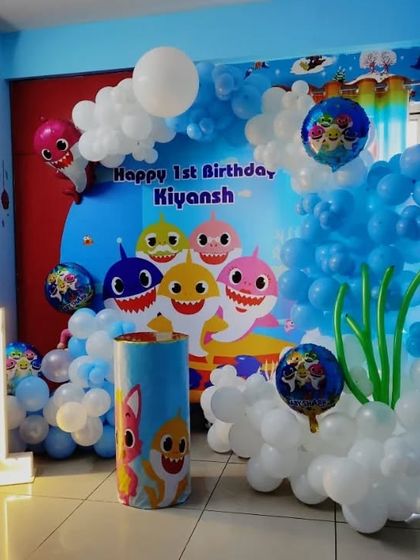 An underwater adventure with this Baby Shark first birthday theme. The setup includes a custom backdrop with the whole shark family, balloon bubbles in blue and white, and a light-up number "1."