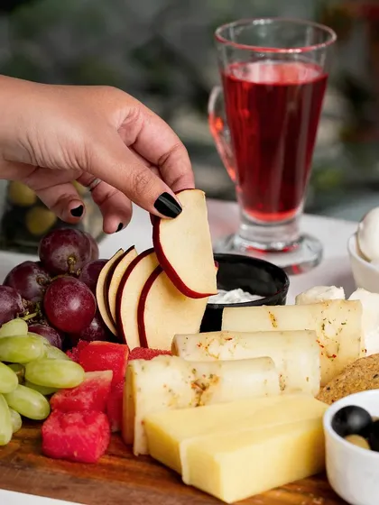 A lifestyle shot of a hand picking an apple slice from a cheese board. Including a human element makes the scene more engaging and relatable.