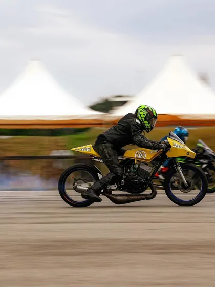 A classic yellow two-stroke race bike, likely a modified Yamaha RX, competing on the strip. We celebrate all eras of motorsport, from modern superbikes to iconic classics.